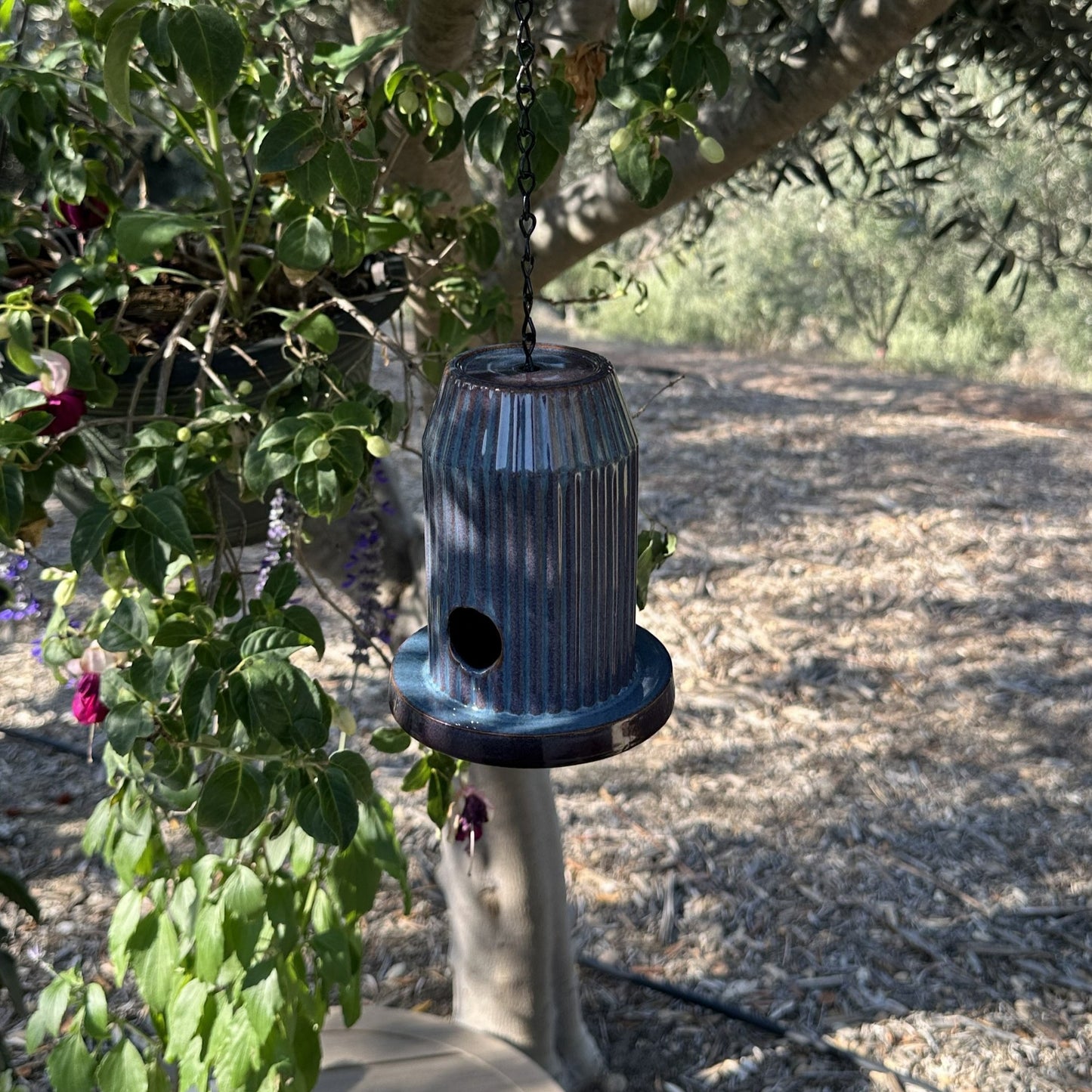 Blue fluted ceramic birdhouse handcrafted from stoneware with black acrylic base, hanging outdoors.