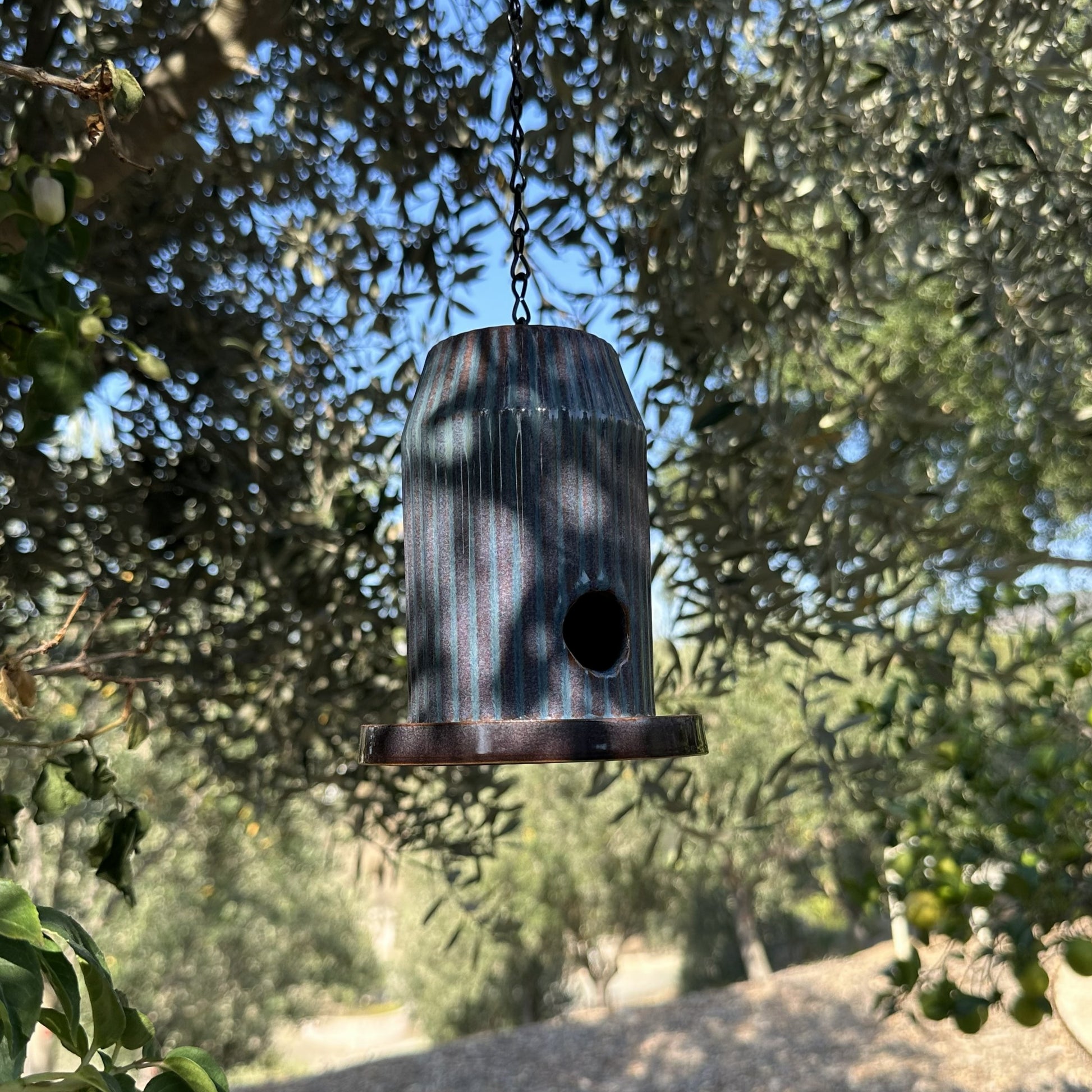 Blue fluted ceramic birdhouse handcrafted from stoneware with black acrylic base, hanging outdoors.