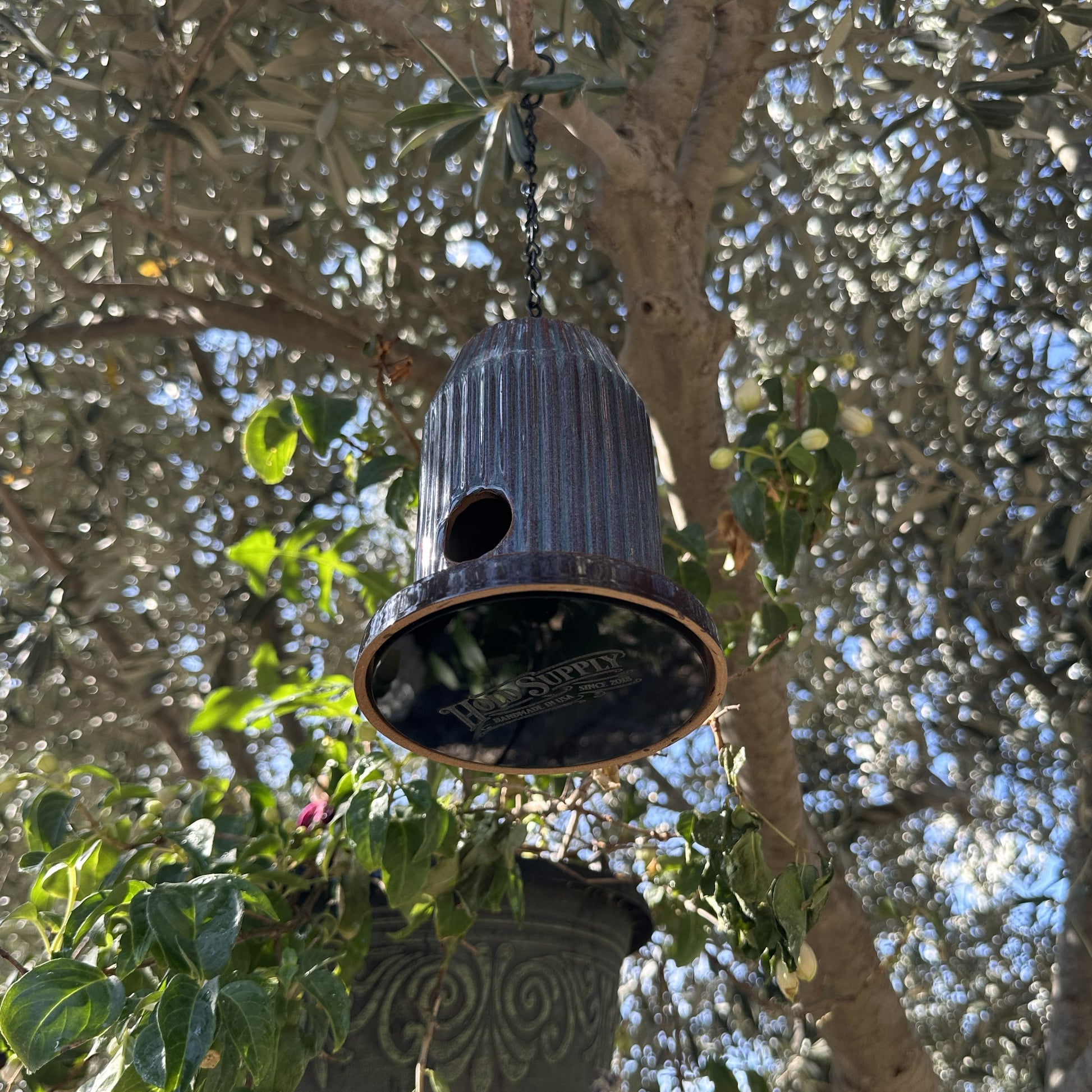 Blue fluted ceramic birdhouse handcrafted from stoneware with black acrylic base, hanging outdoors.