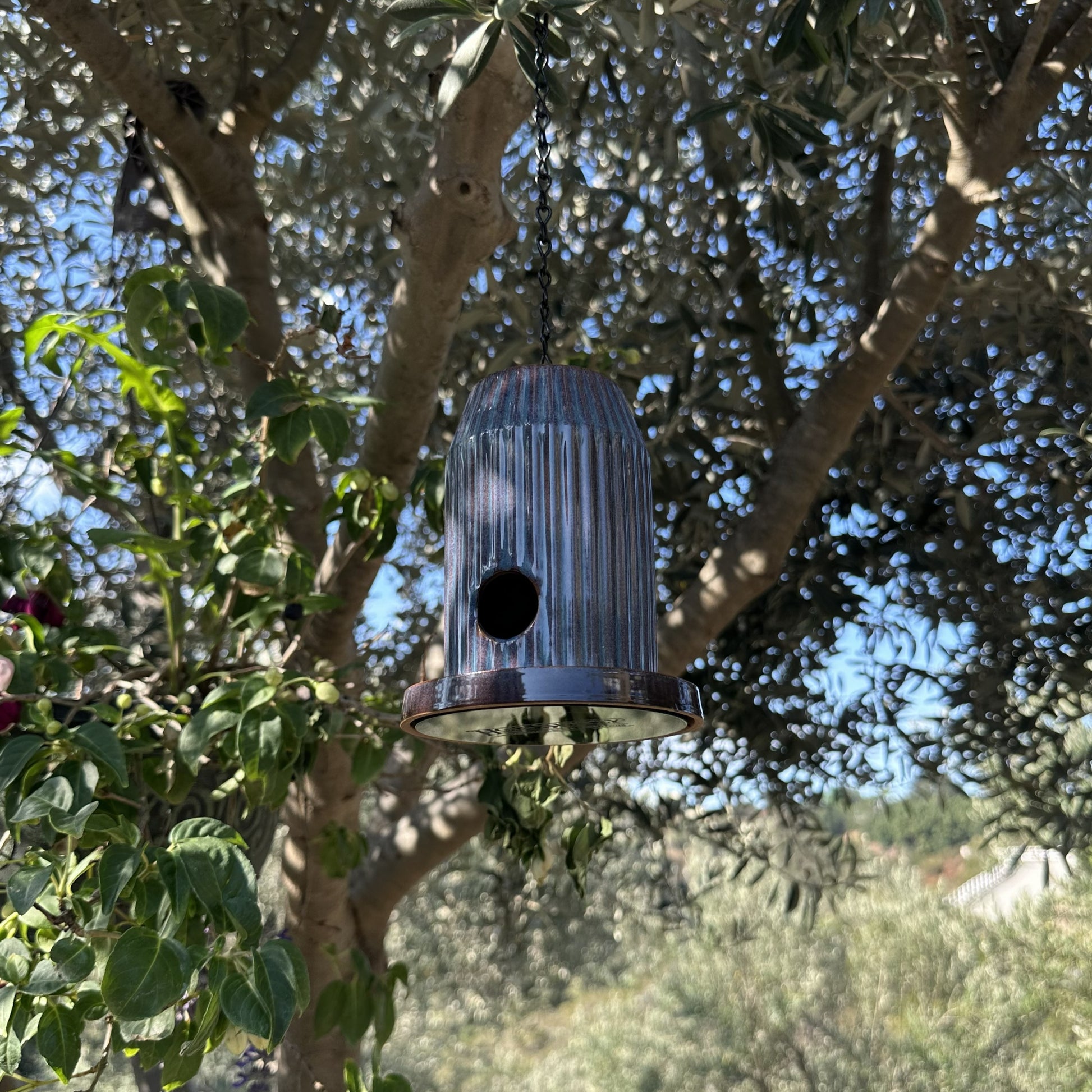 Blue fluted ceramic birdhouse handcrafted from stoneware with black acrylic base, hanging outdoors.