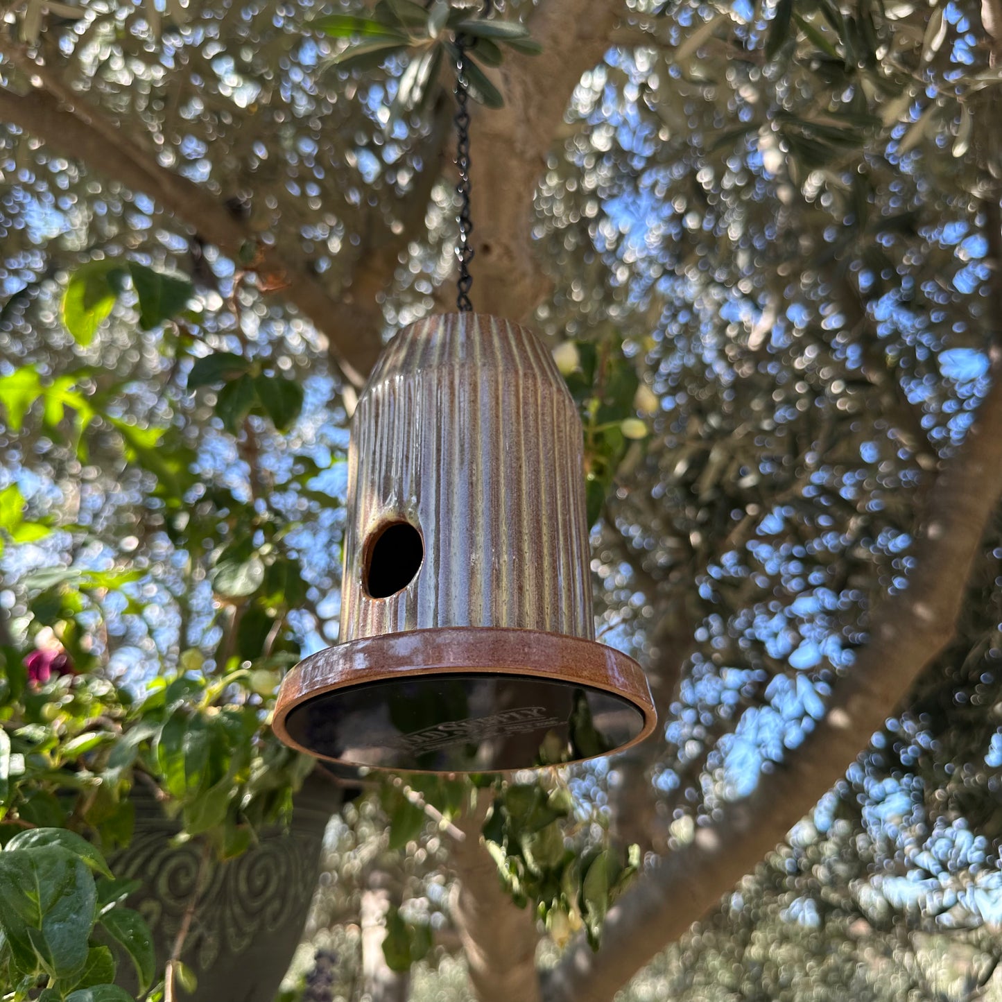 Green fluted ceramic birdhouse handcrafted from stoneware with black acrylic base, hanging outdoors.
