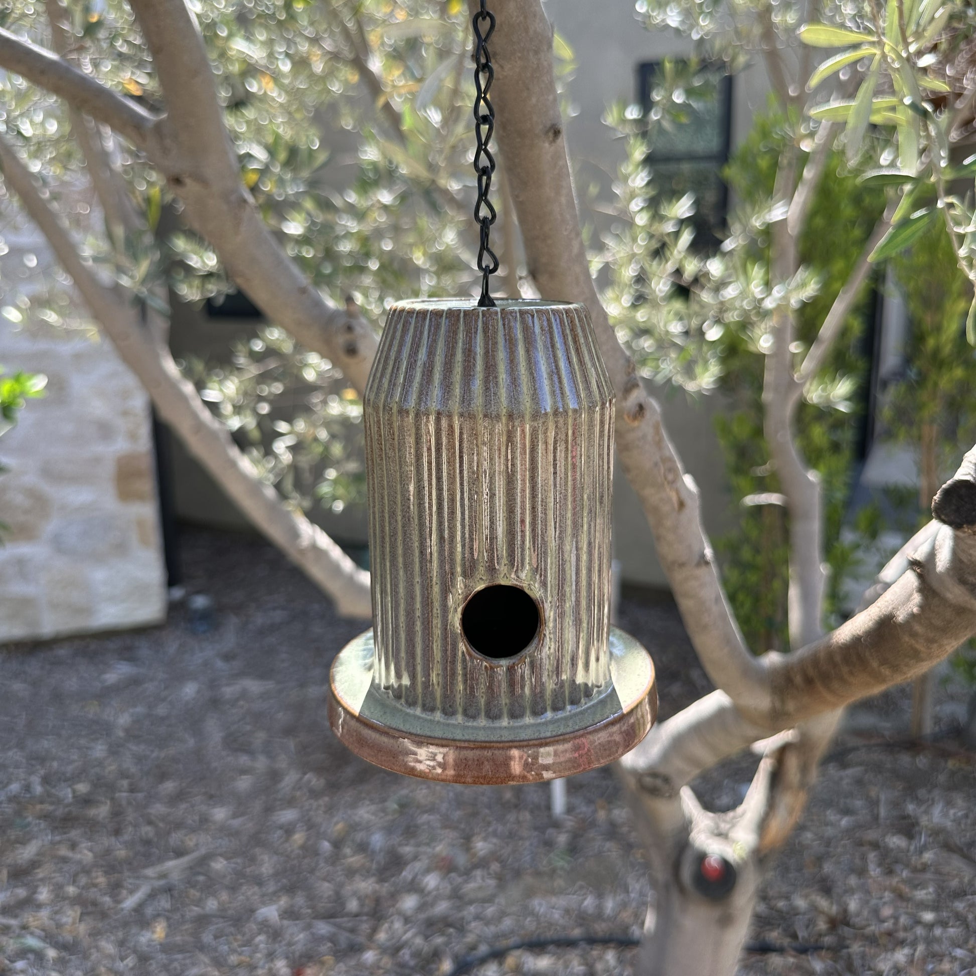 Green fluted ceramic birdhouse handcrafted from stoneware with black acrylic base, hanging outdoors.