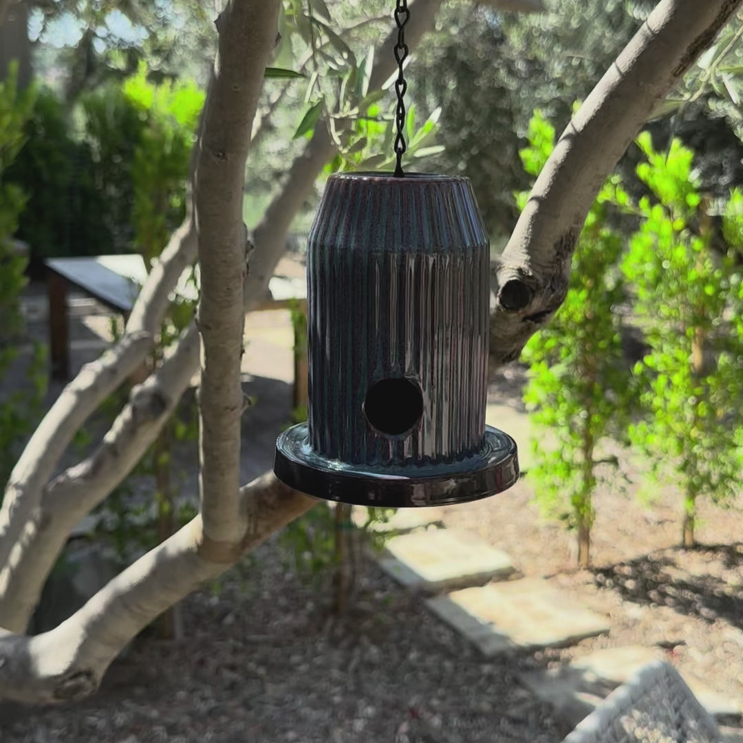 Blue fluted ceramic birdhouse handcrafted from stoneware with black acrylic base, hanging outdoors.